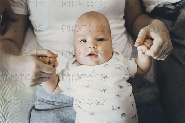 Caucasian mother holding hands of baby son in lap