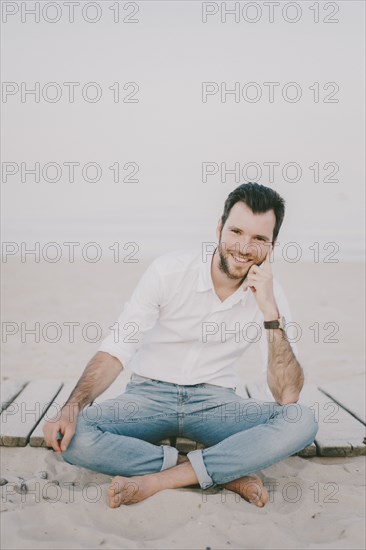 Caucasian man sitting on boardwalk at beach