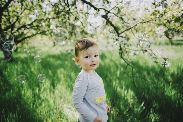 Bubbles floating near Caucasian boy in field near tree