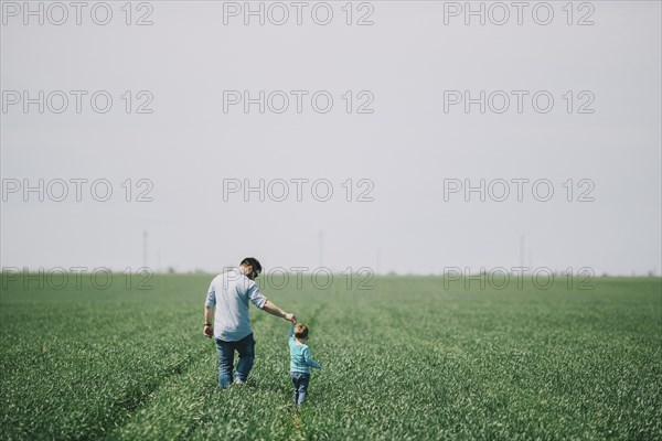 Caucasian father and son holding hands and walking in field