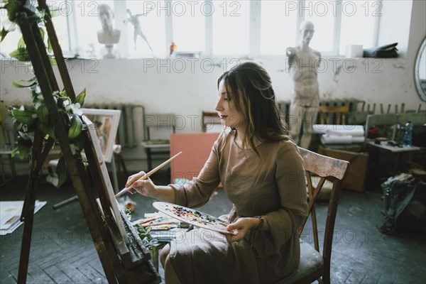 Serious Caucasian woman painting on canvas