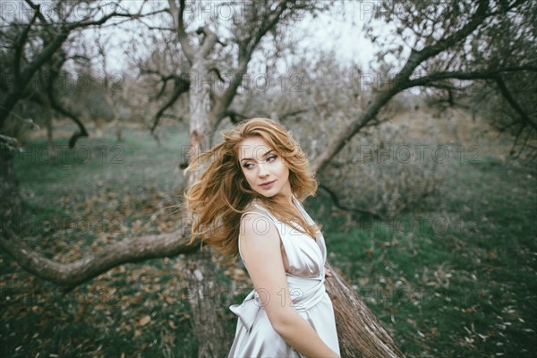 Glamorous Caucasian woman tossing hair near tree