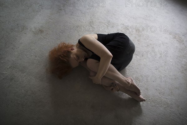 Caucasian woman laying on concrete in fetal position