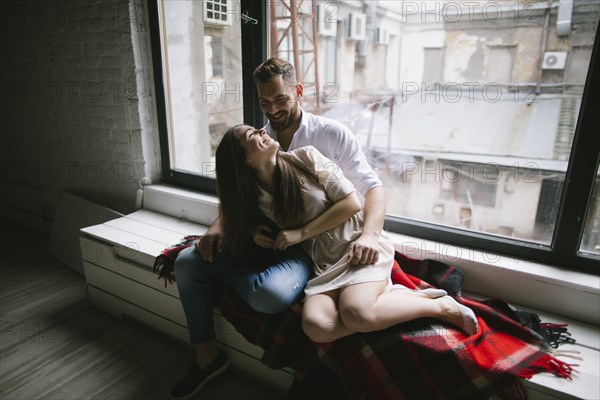 Caucasian couple cuddling on bench near window