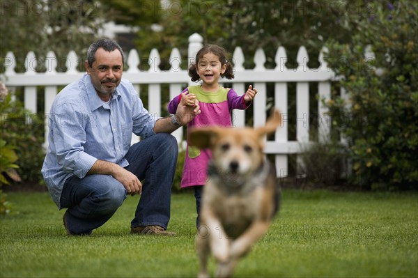 Father and daughter watching dog in backyard