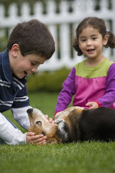 Brother and sister playing with dog in backyard