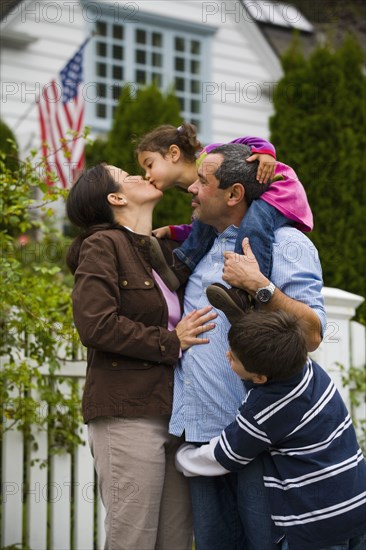 Mother kissing daughter while family watches