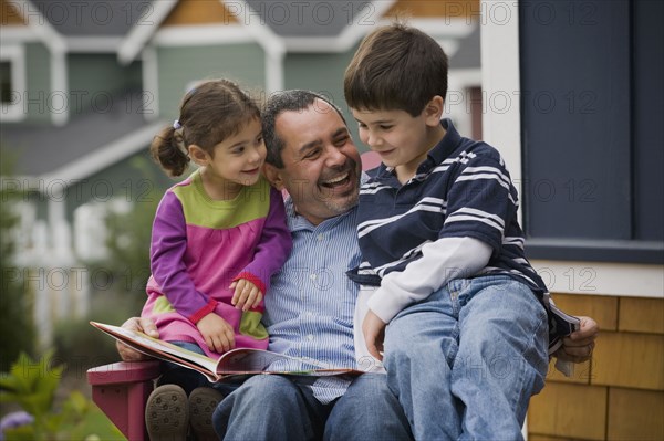 Father reading to son and daughter on porch