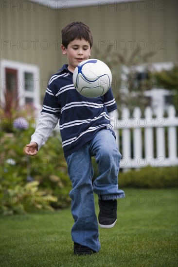 Mixed race boy playing soccer in backyard