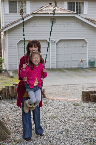 Korean mother pushing daughter on swing