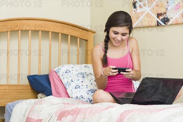 Caucasian teenage girl with laptop text messaging on cell phone