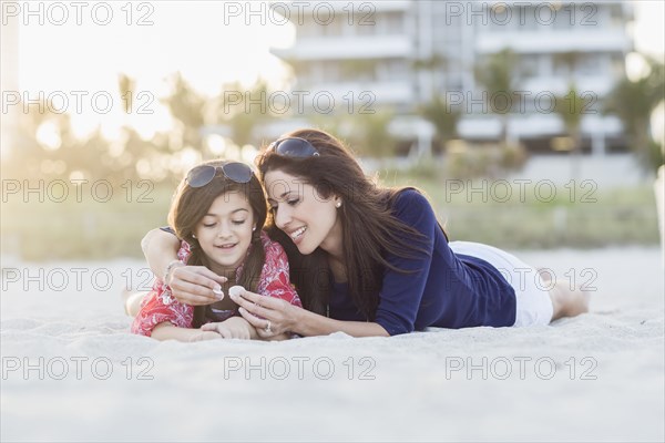 Hispanic mother and daughter laying on beach