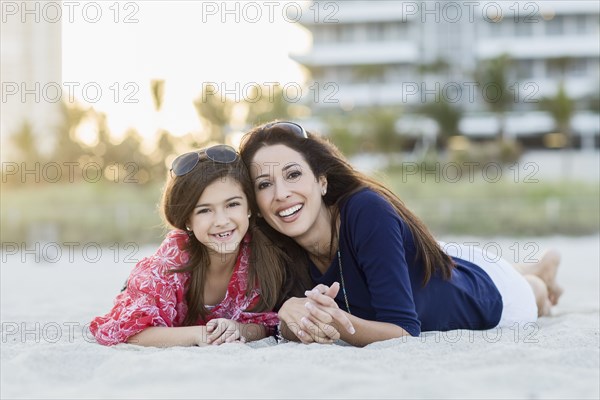 Hispanic mother and daughter laying on beach