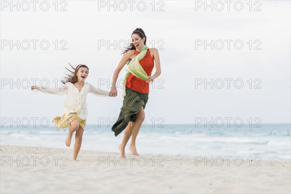 Hispanic mother and daughter running on beach