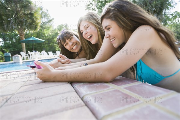 Caucasian teenagers looking at cell phone at poolside