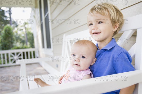 Caucasian brother and sister sitting on porch