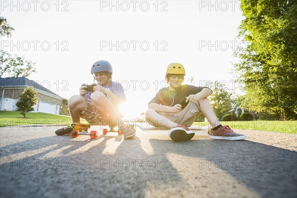 Caucasian boys sitting on skateboards and using cell phones