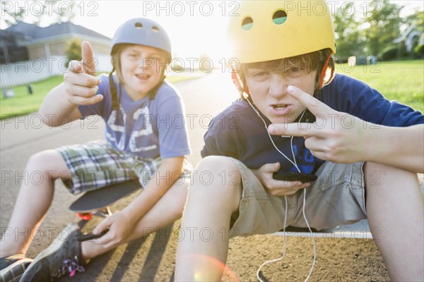 Caucasian boys sitting on skateboards and making gestures
