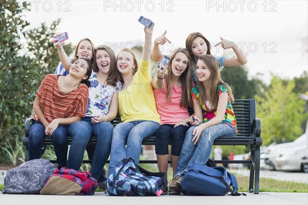 Friends on bench taking self-portraits with cell phones