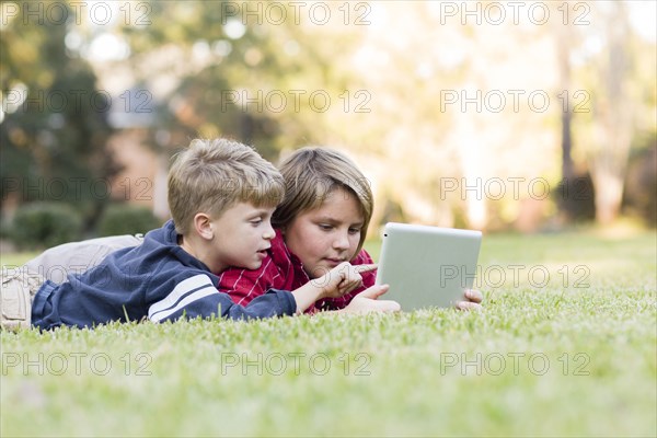 Caucasian boys using digital tablet on lawn