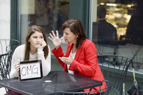 Caucasian girl with tablet as mother chastises her at cafe