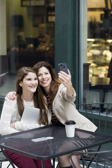 Caucasian mother and daughter taking picture in cafe