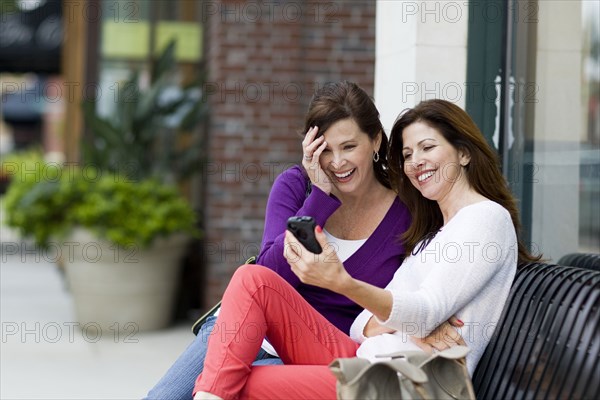 Caucasian women using cell phone on city bench