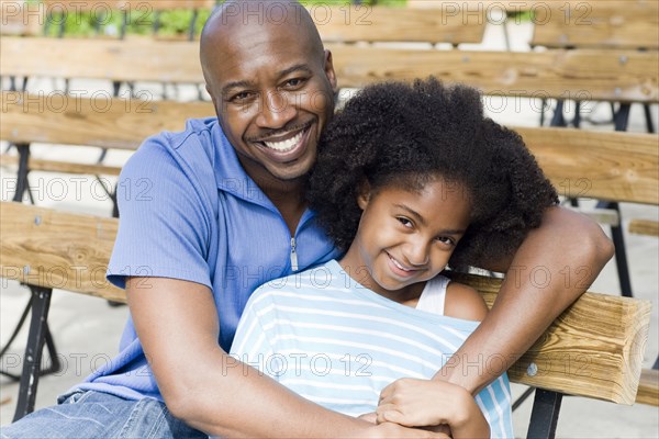 Father and daughter smiling on park bench