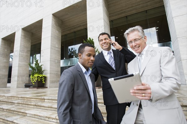 Businessmen using tablet computer on city street