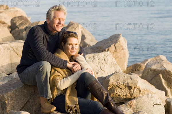 Caucasian couple sitting on rocky beach