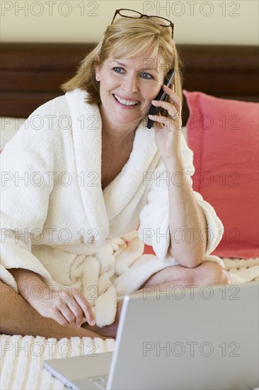 Caucasian woman talking on cell phone on bed