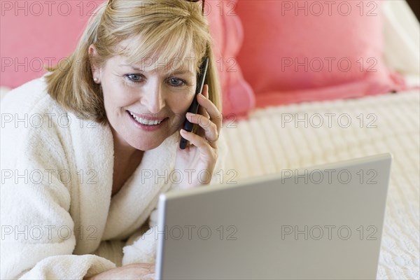 Caucasian woman talking on cell phone on bed