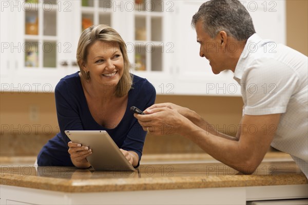 Caucasian couple using digital tablet and cell phone at kitchen counter
