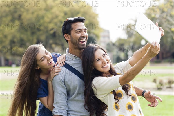 Smiling friends taking photograph with digital tablet in park