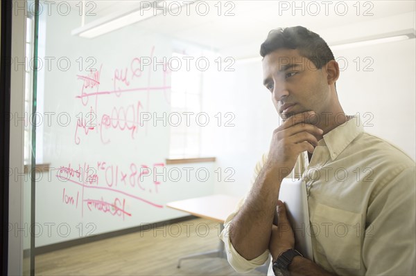 Asian businessman examining writing on glass window in office