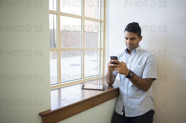 Asian businessman using cell phone and digital tablet at window