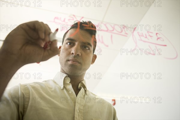 Asian businessman writing formulas on window