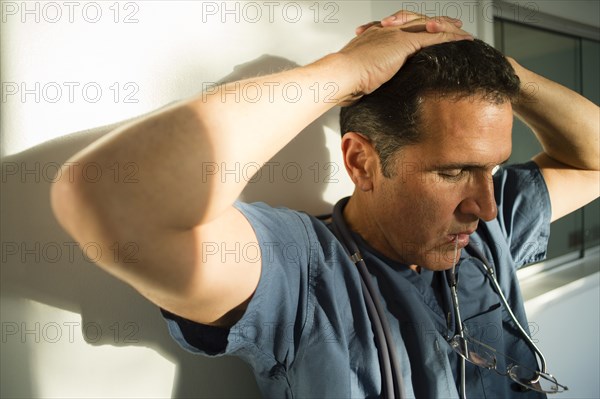 Stressed Hispanic doctor leaning on wall