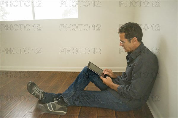 Hispanic man using digital tablet on floor of empty room