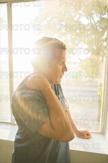 Hispanic doctor rubbing his neck near window