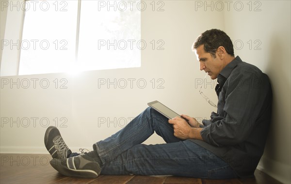 Hispanic man using digital tablet on floor of empty room