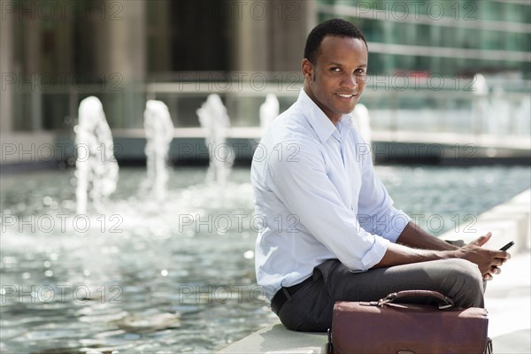 Black businessman using cell phone near urban fountain