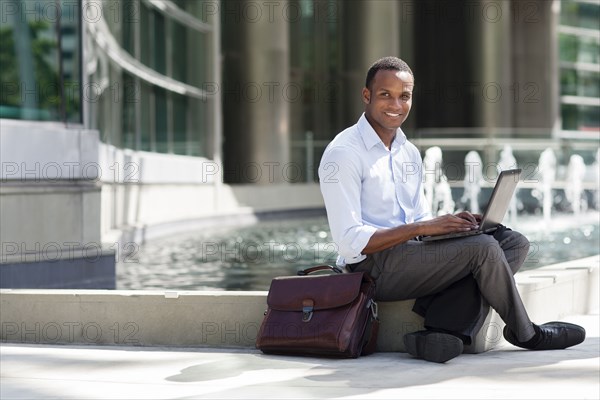 Black businessman using laptop near urban fountain