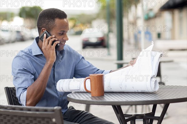 Black architect talking on cell phone and reading blueprints