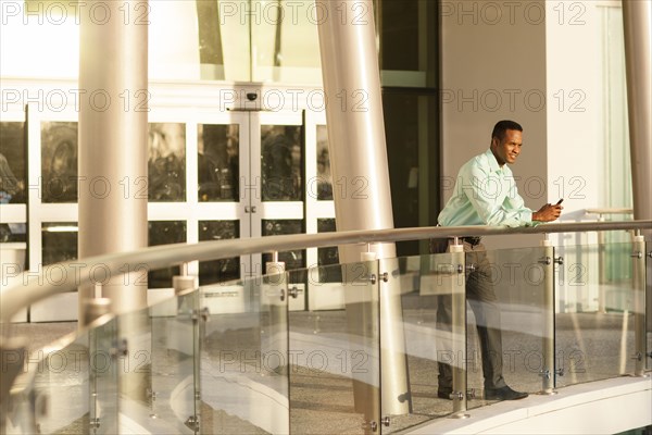 Black businessman using cell phone on railing