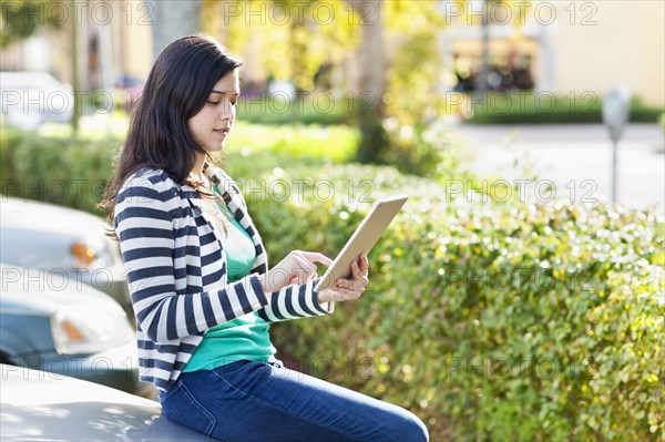Hispanic woman using digital tablet in parking lot