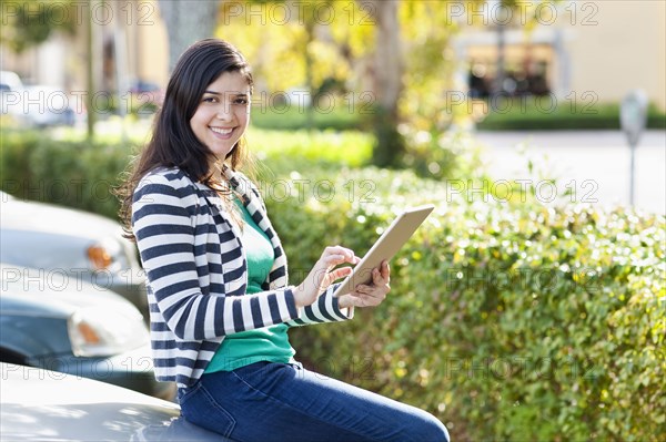 Hispanic woman using digital tablet in parking lot