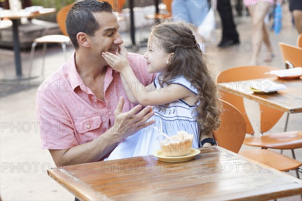 Hispanic father and daughter eating at sidewalk cafe