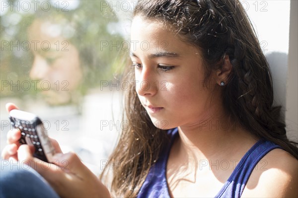 Mixed race girl using cell phone at window