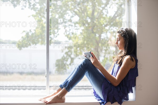 Mixed race girl using digital tablet at window